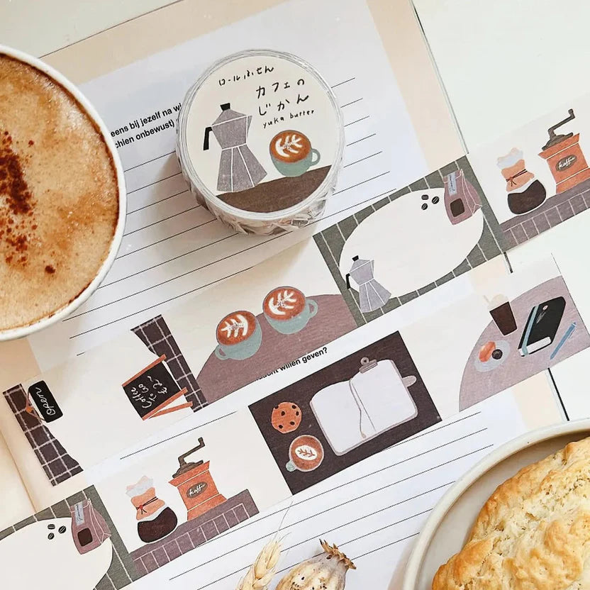 Sticker roll with coffee-themed designs on a notebook with a cup of coffee and pastry.