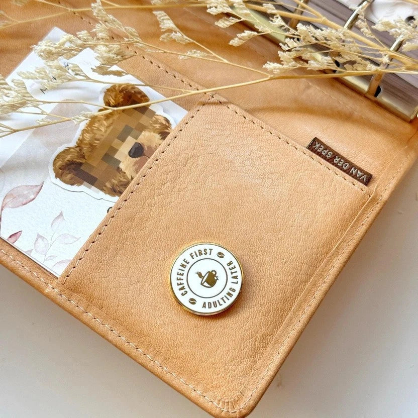 Tan leather wallet with a badge featuring text and a logo, on a light background.