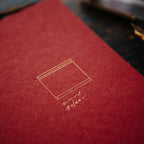 Red leather-bound book with gold embossed design and fountain pen on dark surface