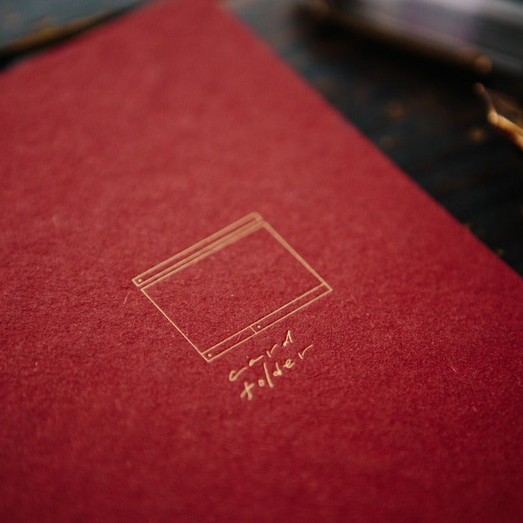 Red Card Folder Notebook with gold embossed cover and a fountain pen on a dark surface