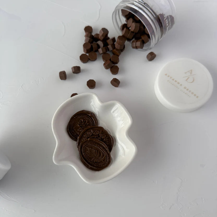 Chocolate Fudge Wax Beads in a white bowl beside the jar of chocolate-brown beads on a grey background