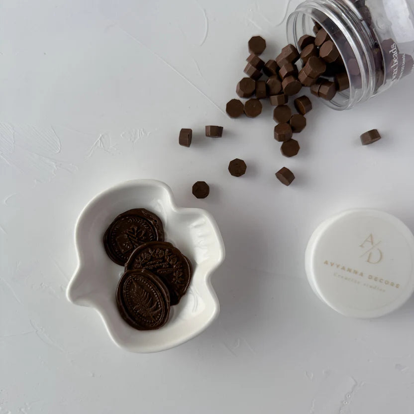 Chocolate Fudge sealing wax beads in a white heart-shaped bowl with beads scattered on light grey
