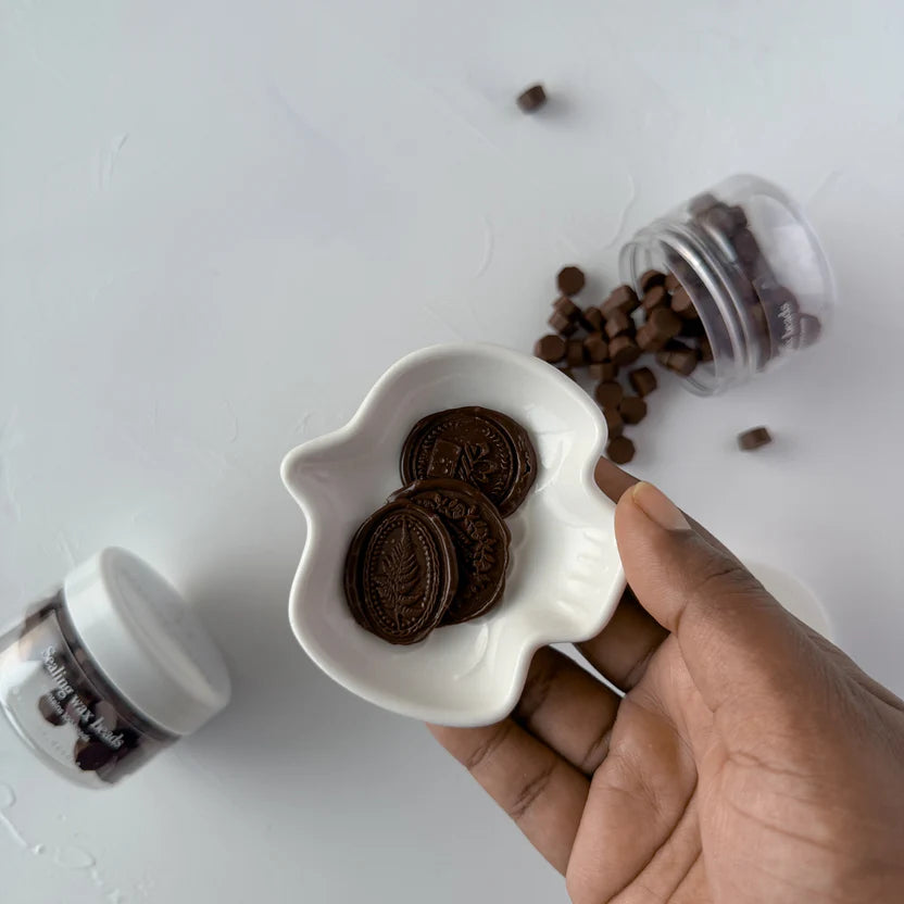 Hand holding a dish of rich brown Chocolate Fudge wax seals with more pieces on a light surface