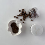 Jar of chocolate cookies with a white dish containing cookies on a light gray background