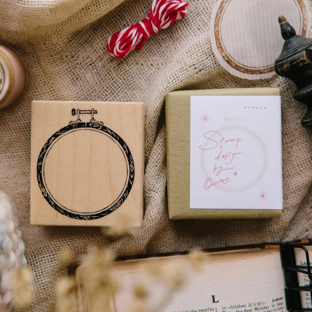 Wooden stamp with circular design on a textured surface with packaging and decorative items.