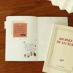 Open book with illustrations on a wooden surface, next to a closed book titled 'Journée de Lecture' by Gallimard.