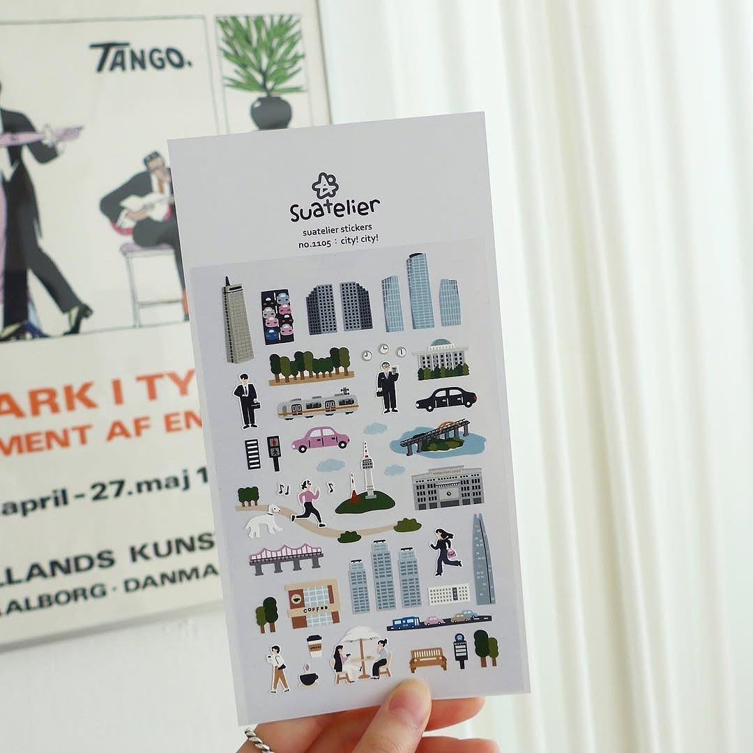 Sheet of Suadeller stickers with city-themed illustrations held by a hand.