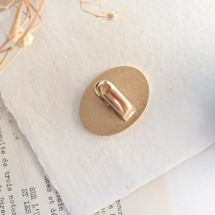 Gold charm detail of the Coffee Journal Clip on a beige base with text in the background