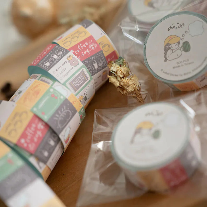 Rolls of Coffee Label Sticker Tape with character label designs displayed on a wooden surface