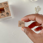 Hand holding a small wooden stamp with a croissant design, with a set of similar stamps in the background.