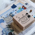 Wooden stamp with a design of a character holding a cup on a decorative background.
