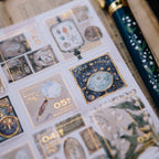 Sticker sheet with celestial designs and a decorative pen on a textured surface.