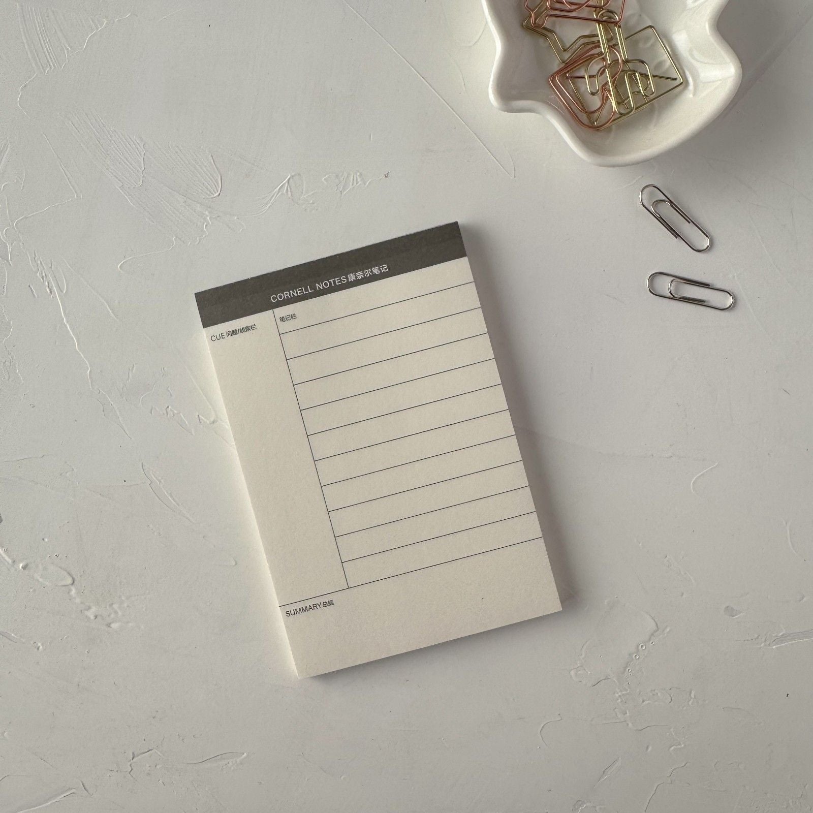 Notebook with lined pages on a light gray surface with paper clips around