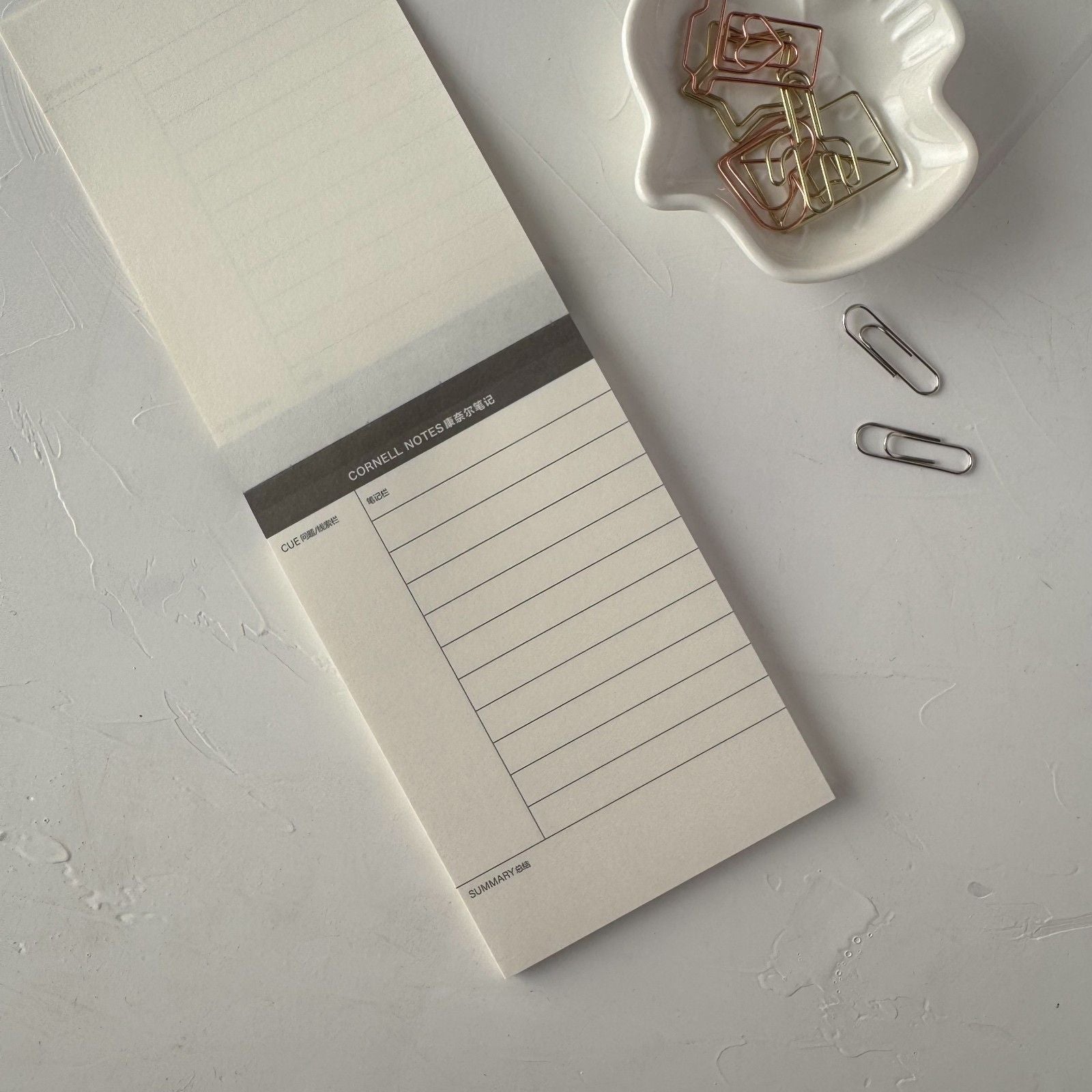 Notebook with a lined page and a plain cover on a light gray surface with paper clips.