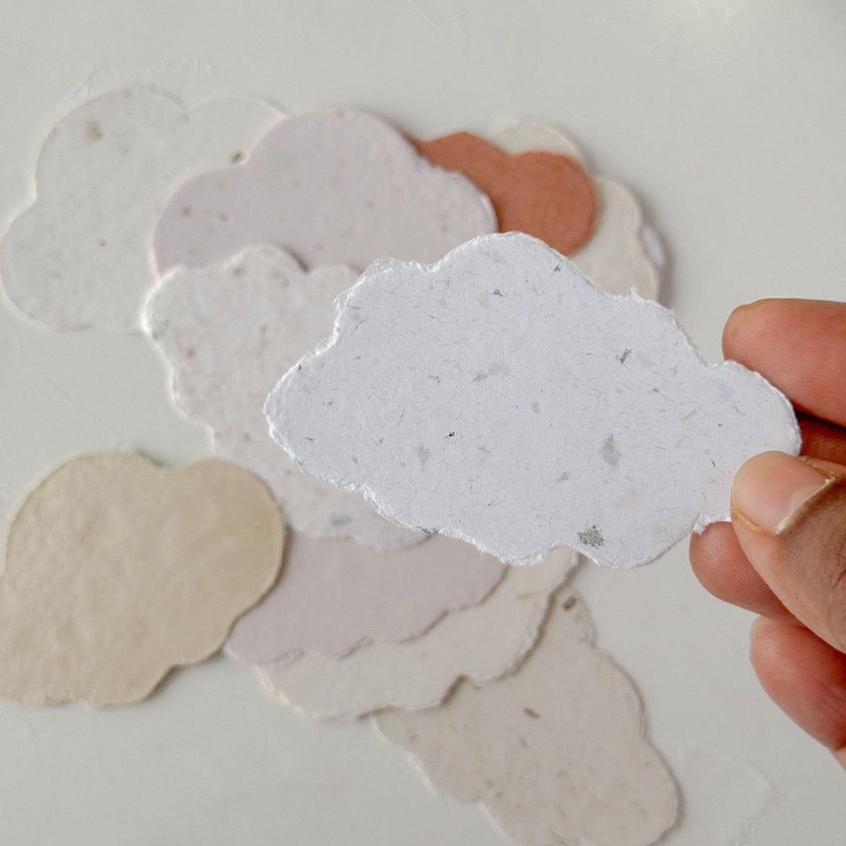 Hand holding a textured white Cotton Cloud Handmade Paper sheet on a light background