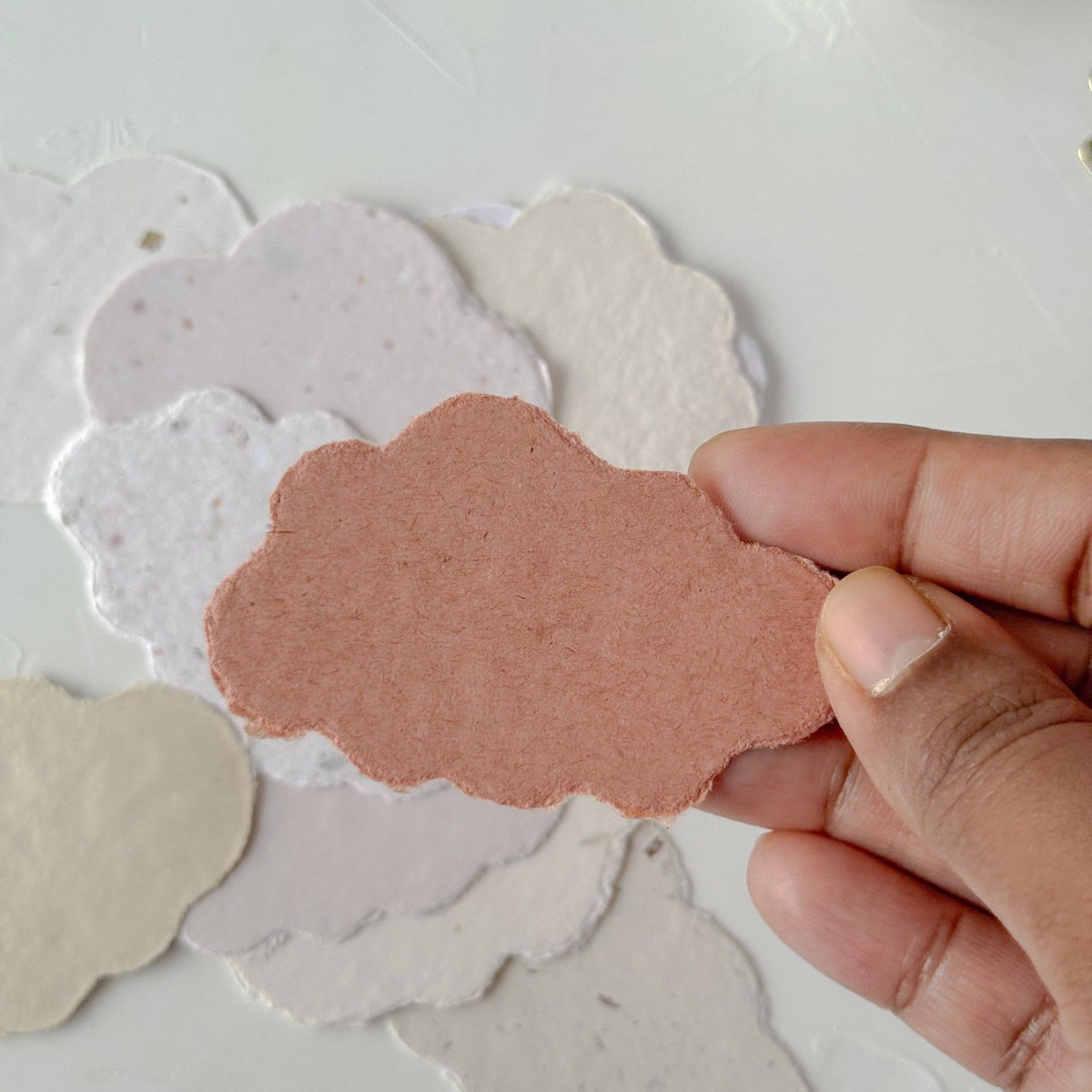 Hand holding a soft pink Cotton Cloud Handmade Paper cloud shape on a light backdrop