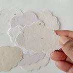 Hand holding a cloud-shaped paper cutout with other similar cutouts on a light background