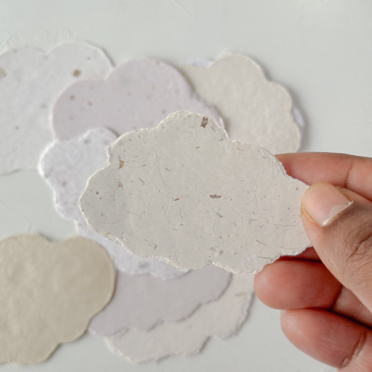 Hand holding a Cotton Cloud Handmade Paper cutout with more cloud shapes visible behind