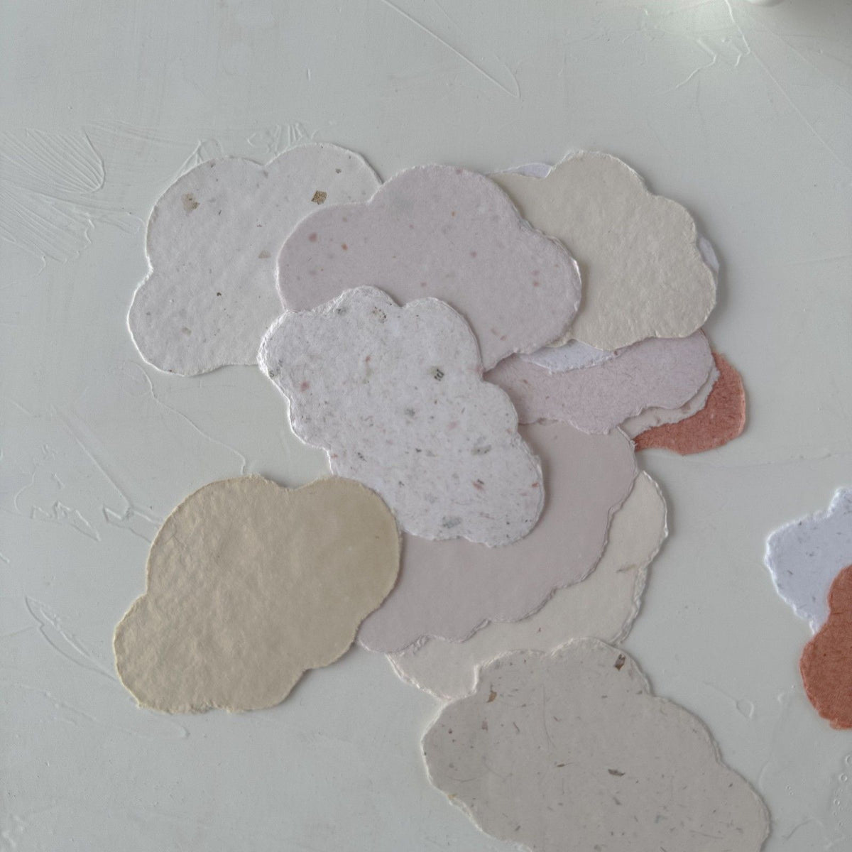 Cloud-shaped Cotton Cloud Handmade Paper pieces scattered on a textured white surface