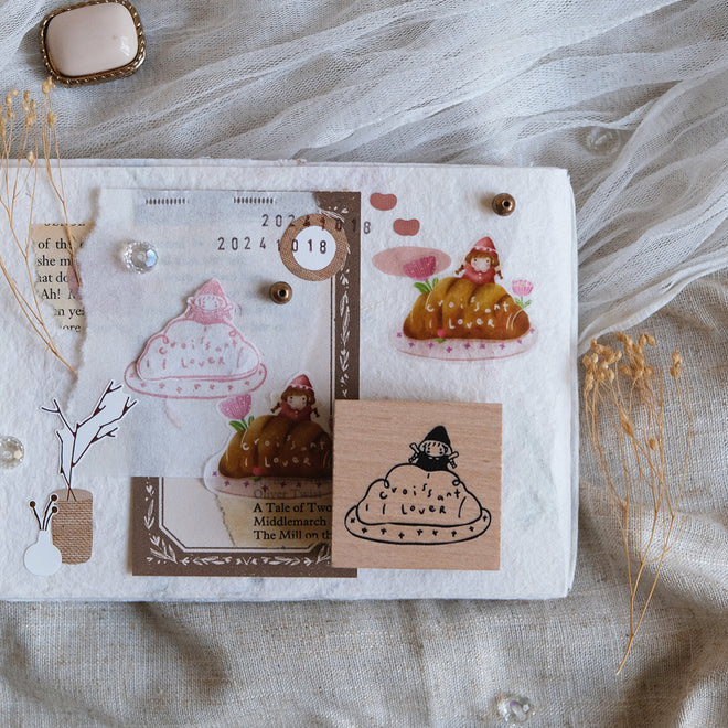 Simple Happiness Croissant Lover stamp beside a small illustrated notebook on textured fabric