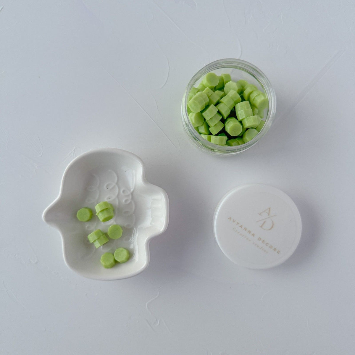 Glass jar of light green Cucumber Cooler sealing wax beads with its white lid on a clean white surface