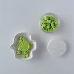 Green candy pieces in a small glass jar and white dish on a light gray background