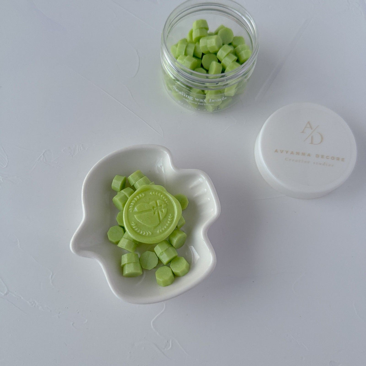 Melted Cucumber Cooler wax seals in a white dish beside the jar of green beads, top-down studio view