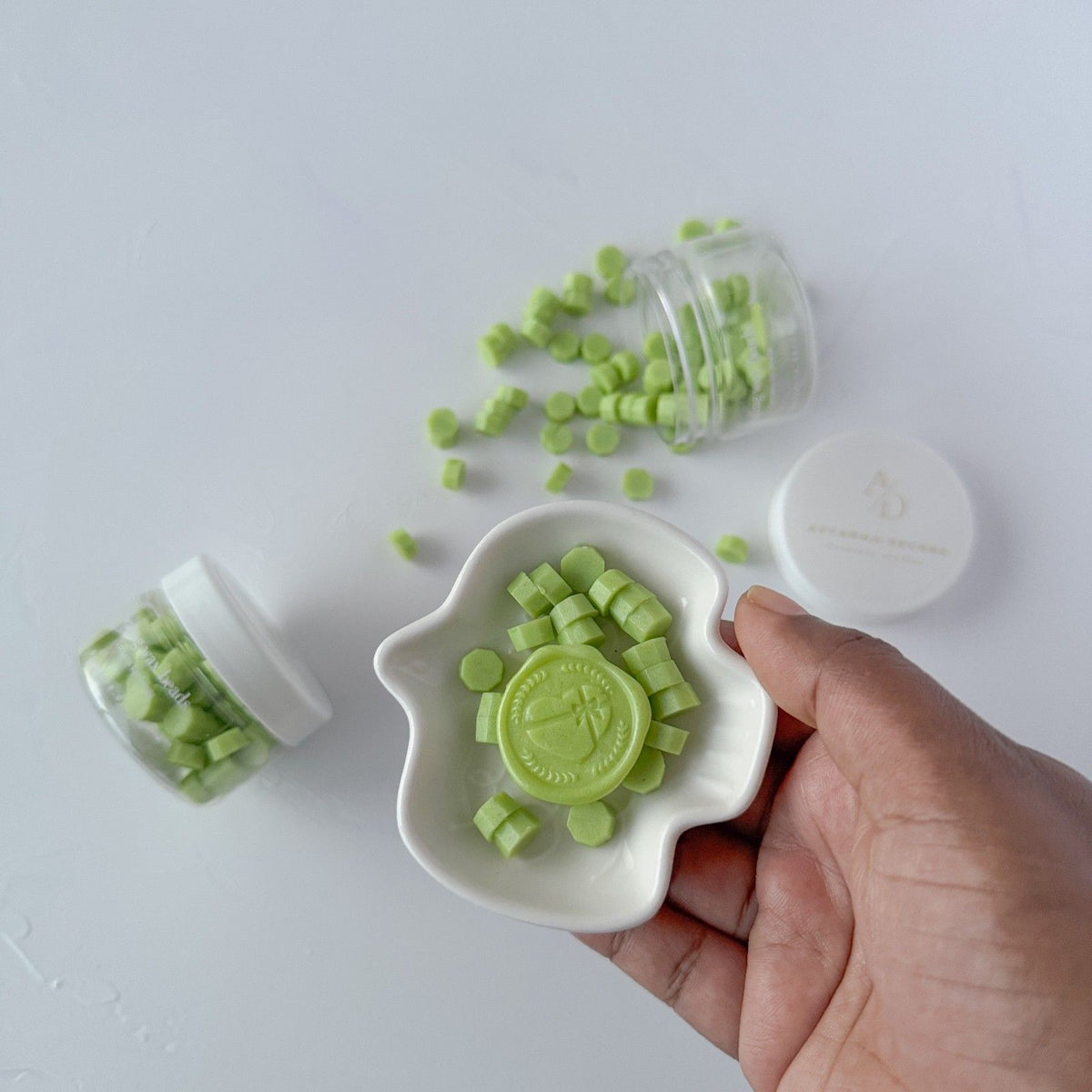 Hand holding a white mold filled with green Cucumber Cooler sealing wax beads on a grey background