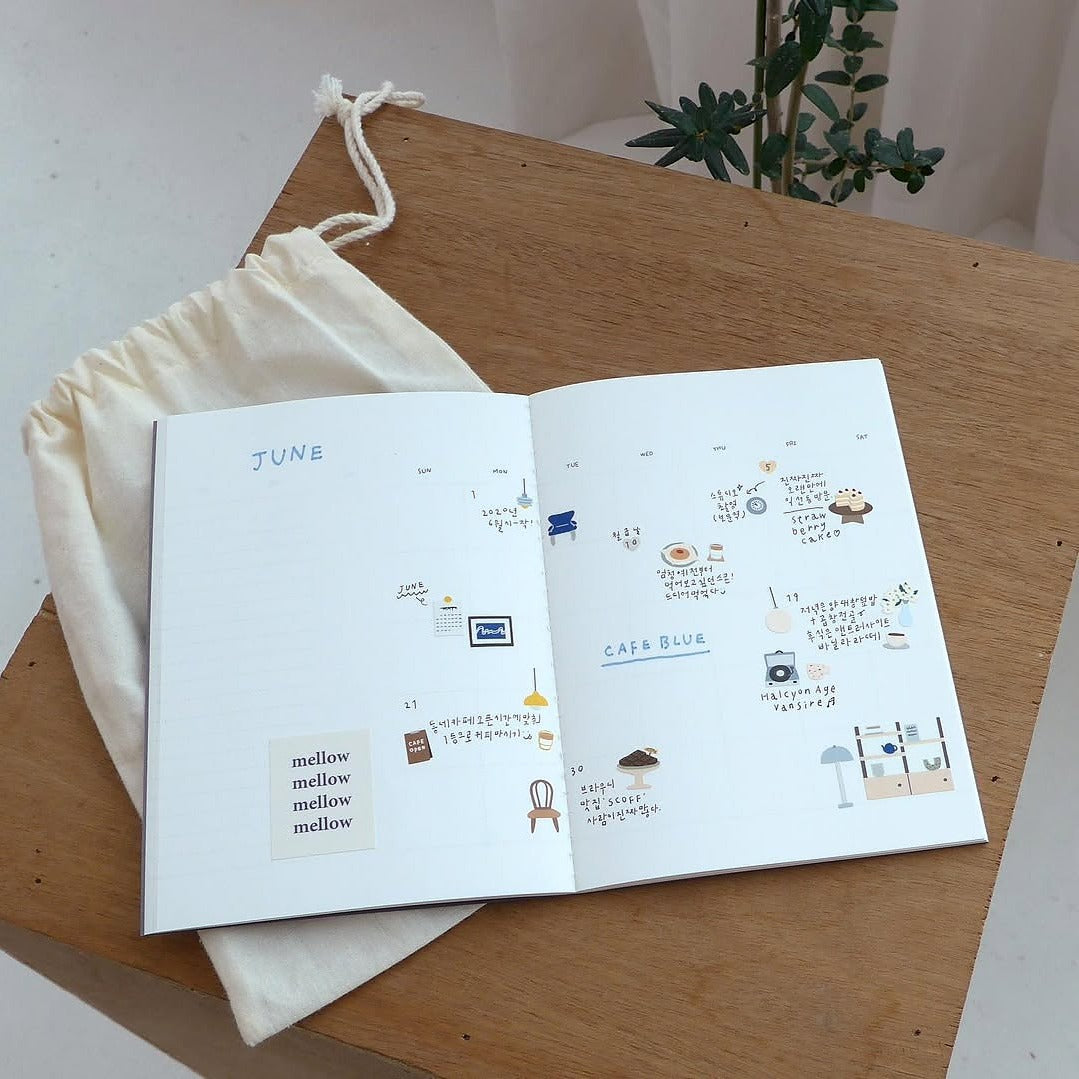 Open book with illustrated pages on a wooden surface, from the Café Blue Sticker Sheet