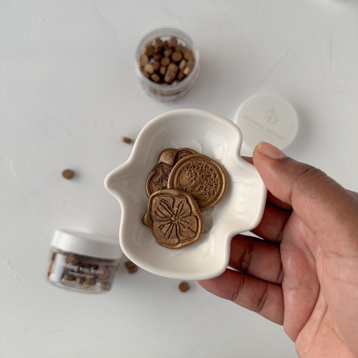 Hand holding a white ceramic dish of earthy Desert Shrub Wax Beads against a light neutral background