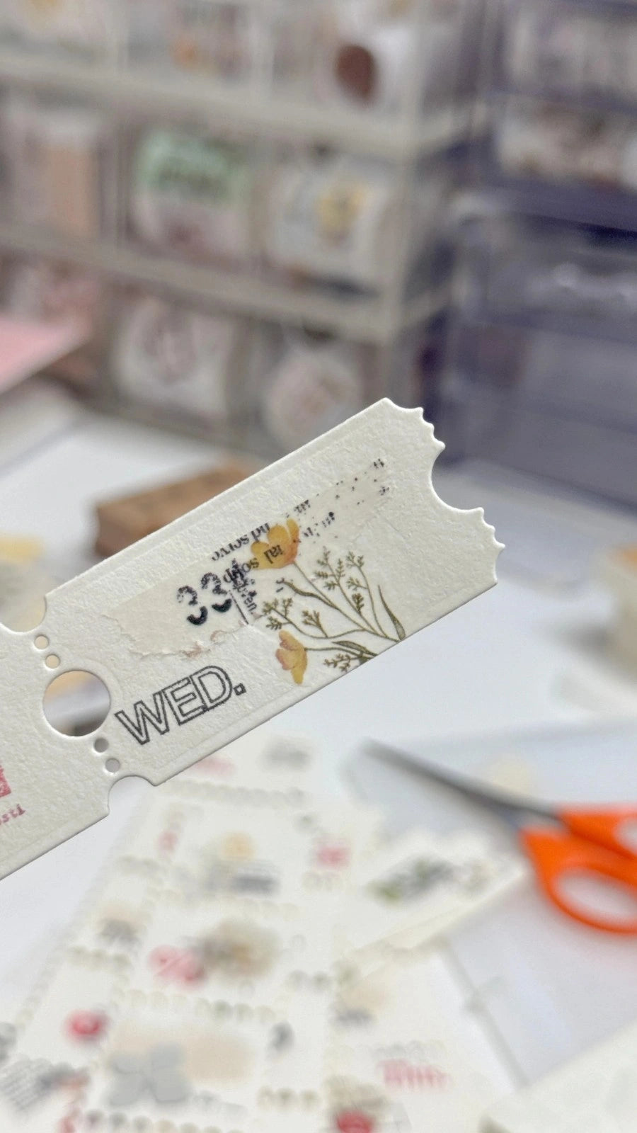 Decorative paper cutout with 'WED.' text on a blurred craft supplies background