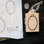 Wooden stamp with oval design on a dark surface next to a piece of paper with printed text.