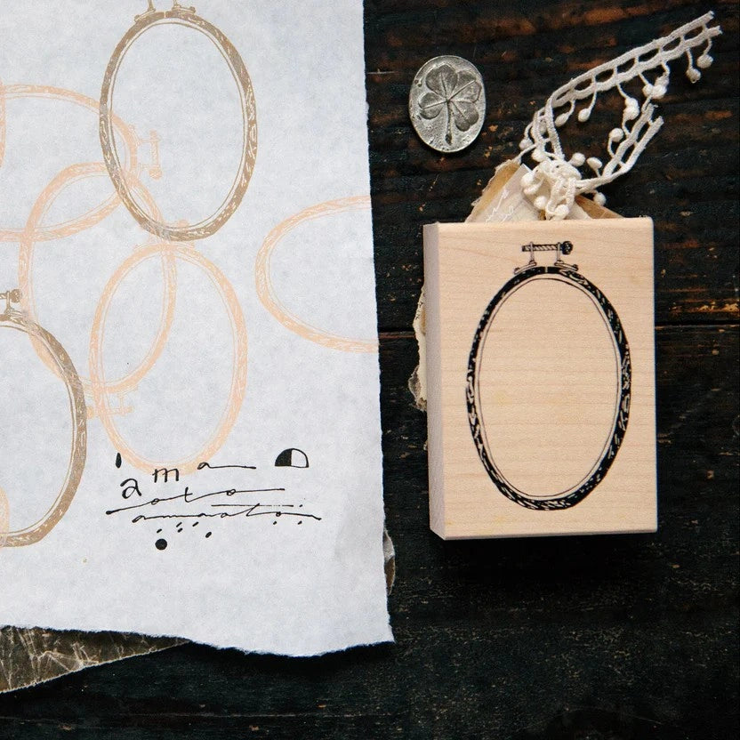 Wooden stamp with oval design on a dark surface next to a piece of paper with printed text.