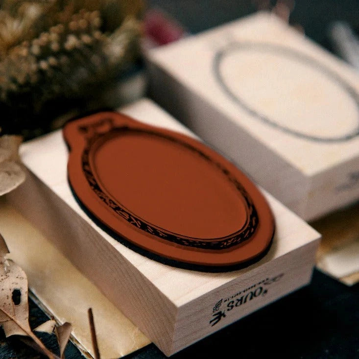 Ellipse Embroidery Hoop Rubber Stamp resting on a white box with a floral blurred background