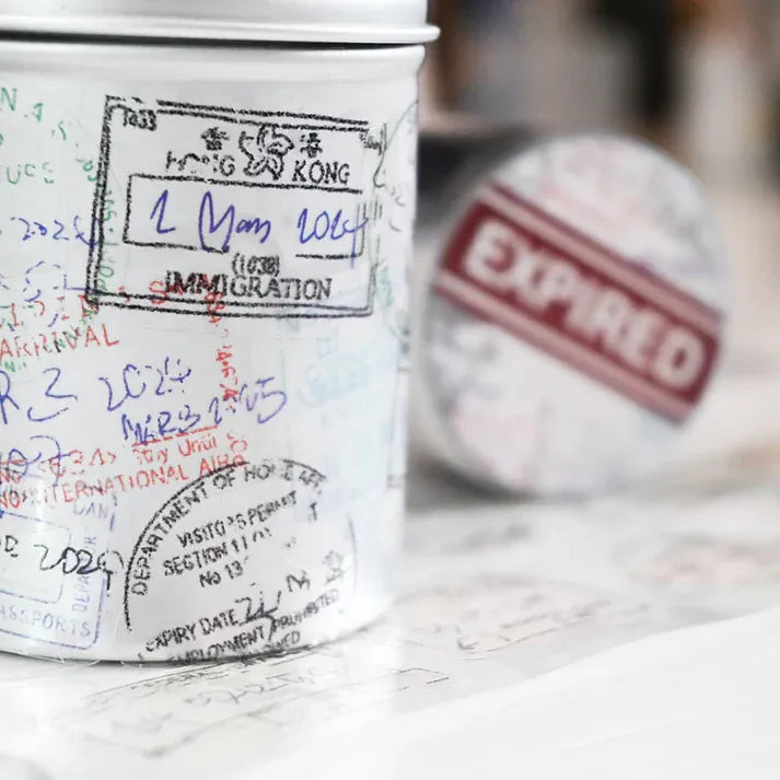 White dispenser of Expired Visa Stamp PET Tape with travel stamp designs on a warm wooden surface