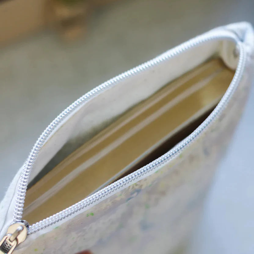 Close-up of a white zipper pouch with a floral pattern on a blurred background