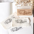 Wooden stamp with 'First Class Mail' design on a white surface with paper and dried flowers.
