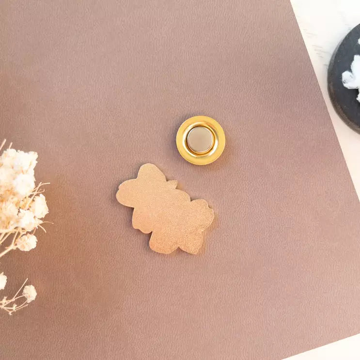 Gold flower-shaped Floral Magnetic Charm and magnet on pink with white flowers alongside