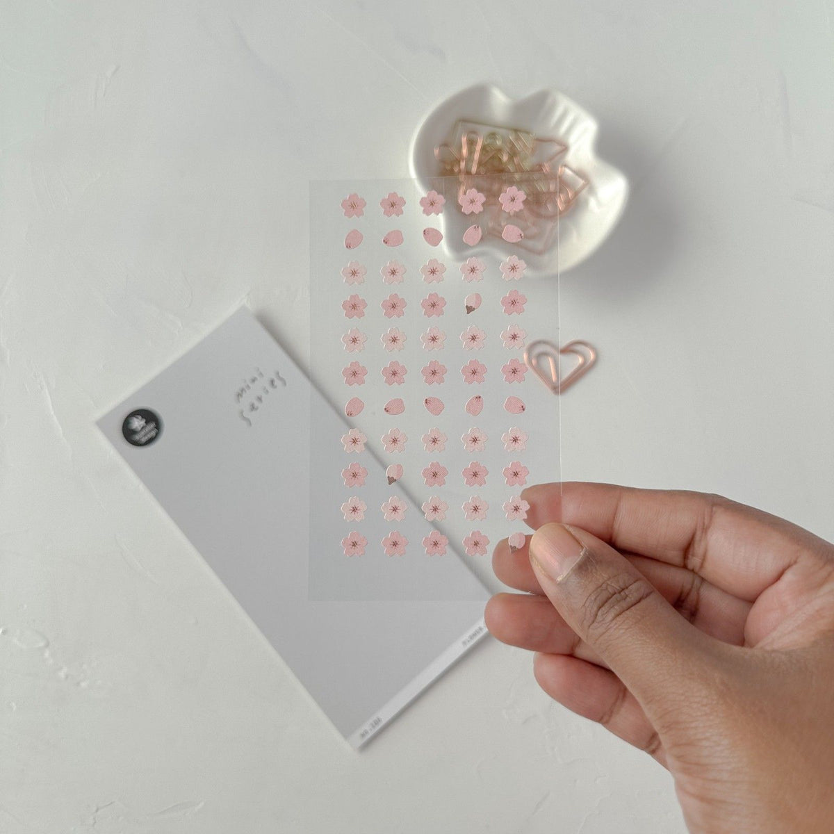 Hand holding a pink heart-shaped paper clip with a container of more clips, from the Flower 01 Sticker Sheet