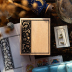 Decorative wooden box with intricate black floral design on a table with cards and other decorative items.