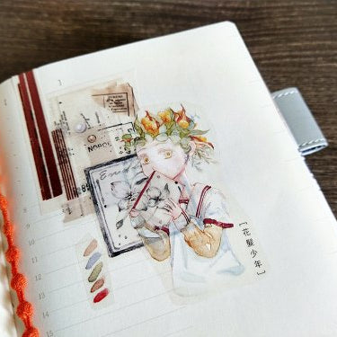 Notebook decorated with Flower Haired Boy PET Tape artistic illustrations on a wooden surface
