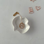 White leaf-shaped trinket dish with a gold necklace, surrounded by rose gold hair clips on a light gray background.