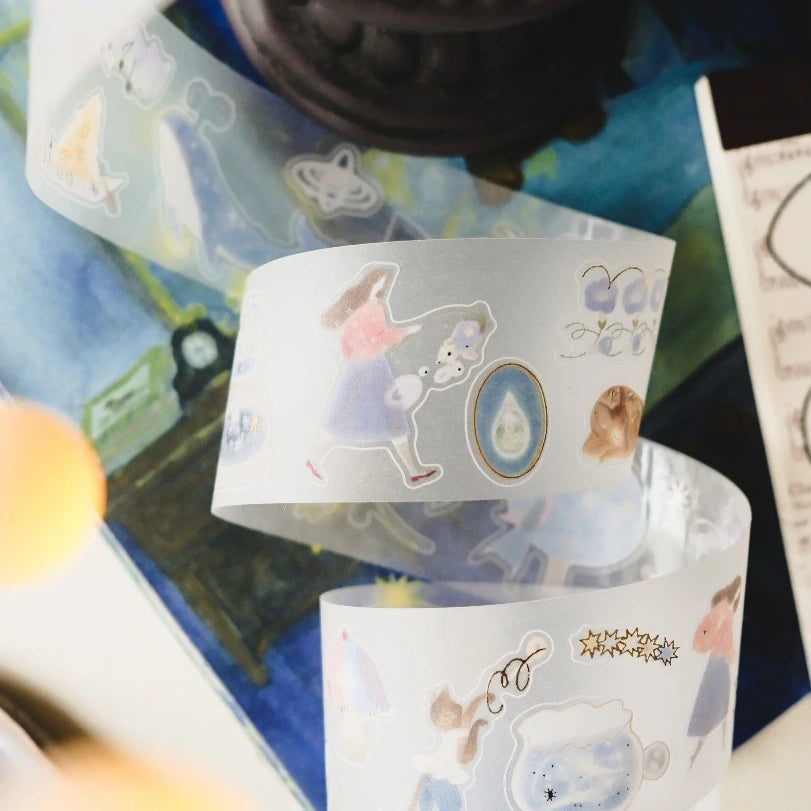 A close-up of a roll of decorative washi tape featuring whimsical illustrated characters and motifs, including a girl in a dress, a rabbit, flowers, and small animals, shown against a softly blurred background.