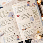 An open handmade planner or journal spread with handwritten notes, decorative illustrations, and small stickers, photographed on a styled surface with warm string lights in the background.
