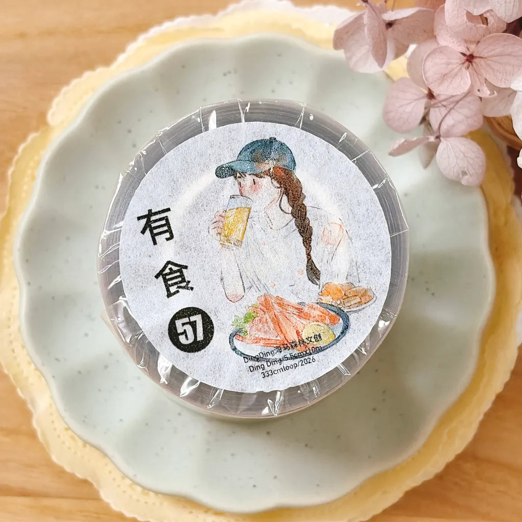 A round clear plastic container with a printed paper lid label, wrapped in clear plastic, placed on a scalloped white plate with a beige lace-like rim. The label shows an illustrated woman drinking and eating, with Chinese text and a black circle containing the number 57.