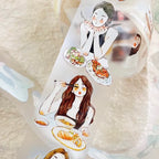 A roll of decorative adhesive tape featuring watercolor-style illustrations of young women dining at tables with plates of food, photographed on a soft cream fabric background.