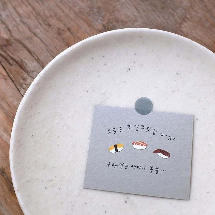 White ceramic plate with a gray card featuring sushi illustrations on a wooden surface