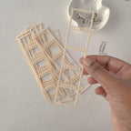 Hand holding a set of decorative lace-like earrings on a light gray background