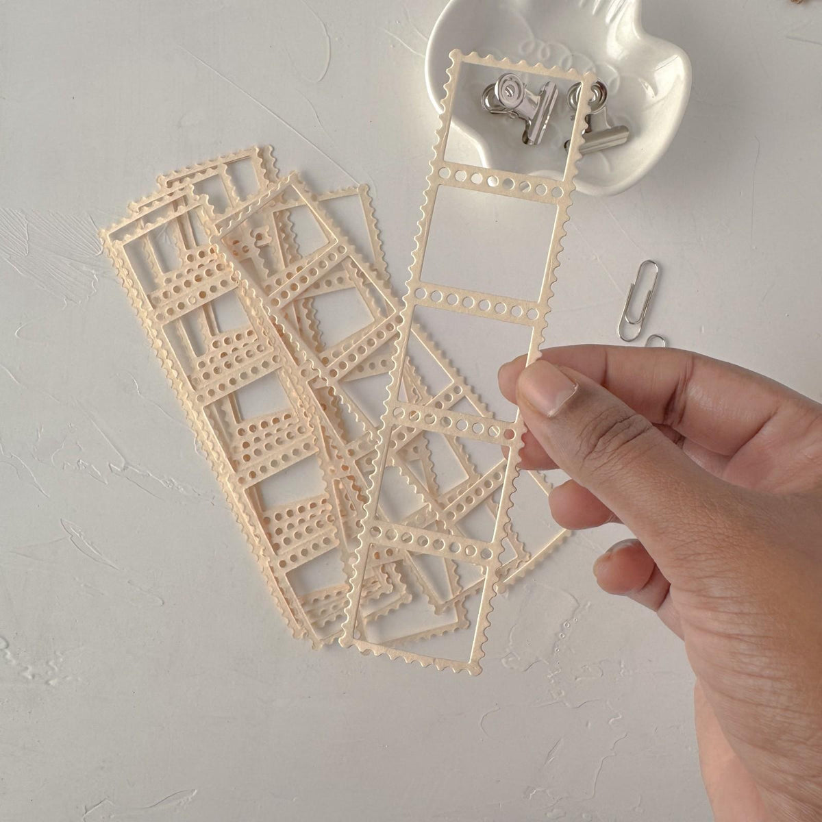 Hand holding delicate cream Frames Vol. 1 lace-style frame cards on a light grey backdrop