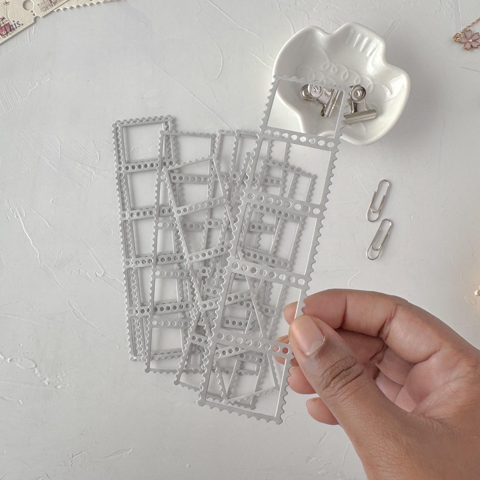 Metal die cut shapes on a white surface with a hand holding one piece.